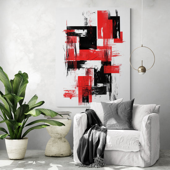 Tableau rouge et noir aux touches graphiques accrochée sur un mur clair. Fauteuil blanc avec coussin et plaid gris. À gauche, grande plante tropicale dans un pot beige. Petite table en pierre avec des livres. Suspension dorée fine.