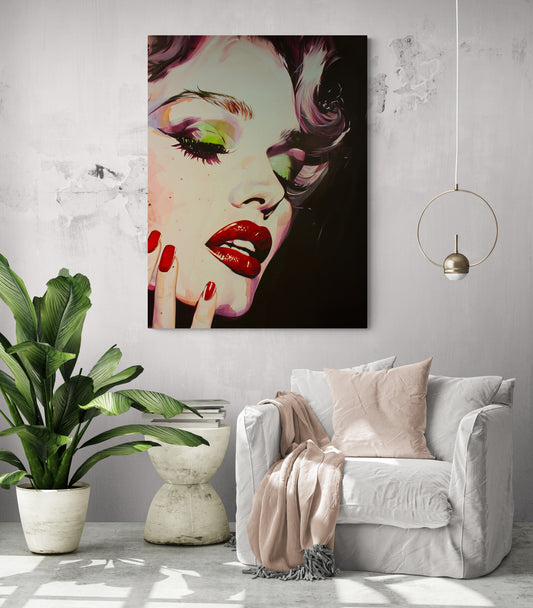Grand tableau Marilyn Monroe, pièce de vie illuminée, fauteuil confortable avec coussin et plaid rose pâle, table d'appoint avec livres, grande plante verte, luminaire suspension.