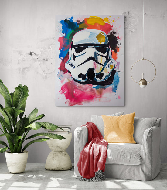 Un intérieur moderne avec un fauteuil blanc, un coussin jaune et une couverture rouge. À côté du fauteuil, une plante en pot. Au-dessus, un tableau coloré représentant un casque de Stormtrooper sur un fond éclaboussé de rouge, bleu, jaune et rose.