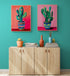 Deux tableaux colorés de cactus sont accrochés au-dessus d'un buffet moderne en bois clair, apportant une touche artistique vivante à un salon aux murs turquoise