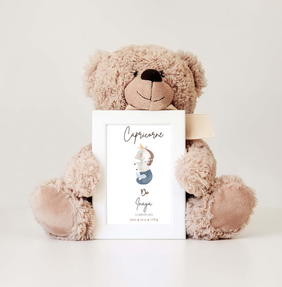 Un adorable ours en peluche tient un cadre avec un tableau personnalisé du signe Capricorne, représentant une petite licorne accompagnée des détails de naissance du bébé.