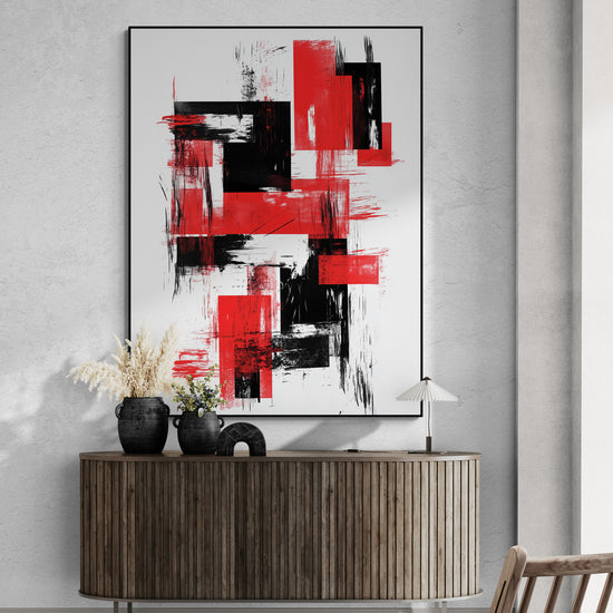 Grand tableau rouge et noir suspendu sur un mur en béton clair. En dessous, meuble bas en bois nervuré. Vases noirs décoratifs, bouquet de fleurs séchées, petite lampe blanche à pied fin. Ambiance épurée et élégante.