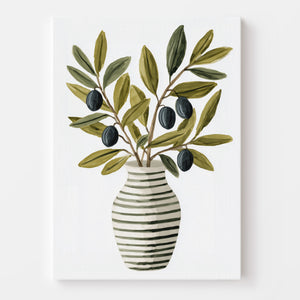 Affiche d’un vase rayé garni de branches d’olivier, mise en valeur dans une cuisine décorée avec des éléments modernes et naturels (plantes, carafe métallique, fruits). L’ensemble évoque fraîcheur et authenticité.
