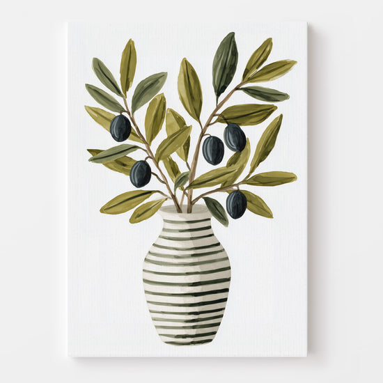Affiche d’un vase rayé garni de branches d’olivier, mise en valeur dans une cuisine décorée avec des éléments modernes et naturels (plantes, carafe métallique, fruits). L’ensemble évoque fraîcheur et authenticité.