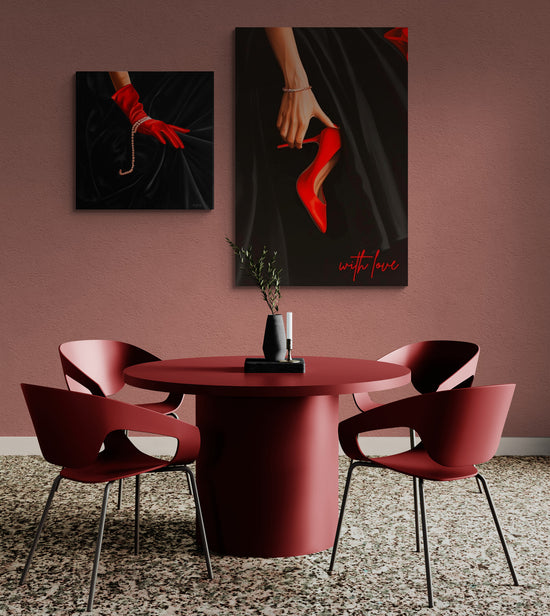 Un espace de salle à manger avec des murs roses et des meubles rouges. Deux tableaux sont accrochés : l'un montrant une main avec un escarpin rouge et l'autre une main avec un gant rouge et un bracelet.