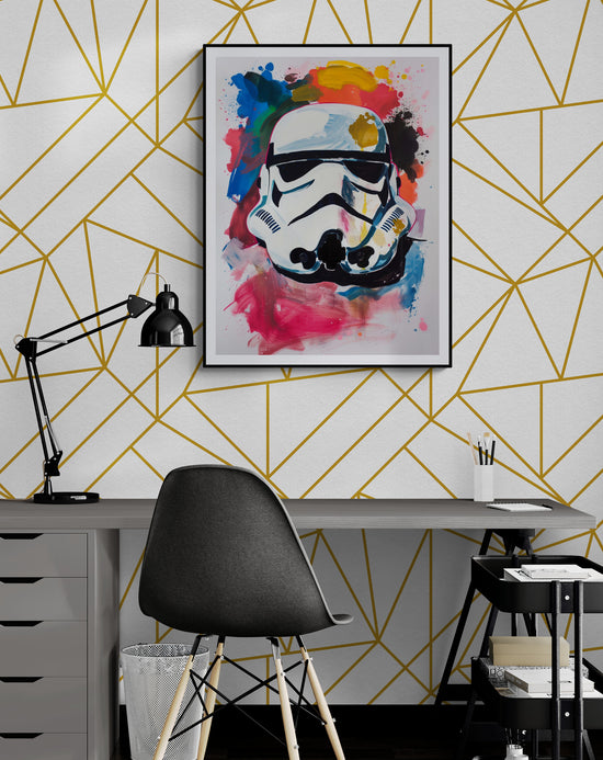 Un bureau moderne avec une chaise noire devant un mur blanc orné de motifs géométriques dorés. Au-dessus du bureau, un tableau coloré représentant un casque de Stormtrooper avec des éclaboussures de rouge, bleu, jaune et rose.