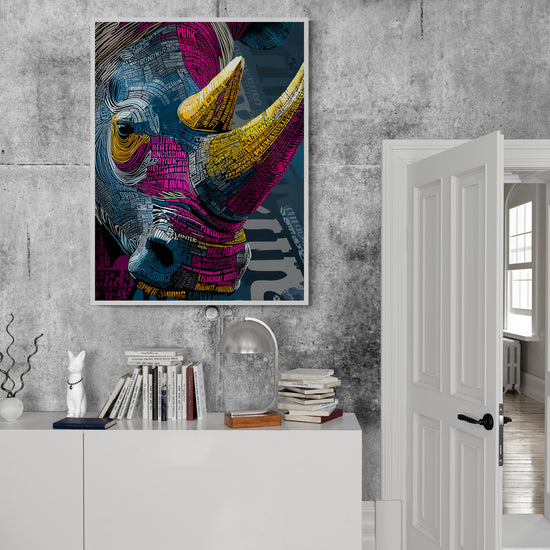 Affiche de rhinocéros accrochée sur mur effet béton. En dessous, meuble blanc avec livres, lampe métal et déco sobre. Porte blanche ouverte sur pièce lumineuse.