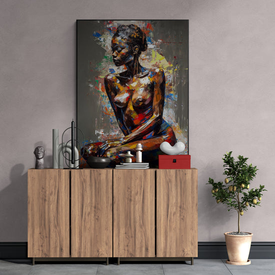 Un buffet bas en bois naturel est placé contre un mur texturé taupe, surmonté d’une composition décorative contemporaine incluant des objets sculpturaux et un tableau éclatant représentant une femme nue peinte dans un style abstrait multicolore. À droite, un petit citronnier en pot apporte une touche végétale à l’ensemble.