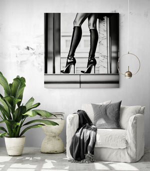 Intérieur contemporain avec un fauteuil blanc, un plaid foncé et un tableau en noir et blanc représentant des jambes féminines en talons aiguilles et chaussettes montantes. L’image joue sur l’élégance urbaine et le contraste graphique, créant une ambiance chic et audacieuse