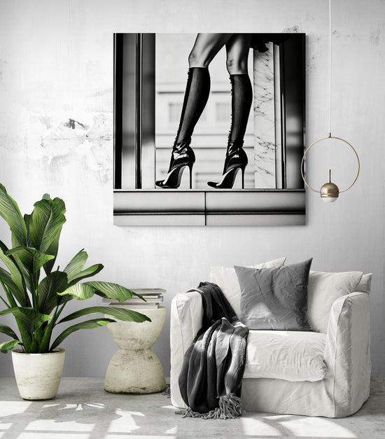 Intérieur contemporain avec un fauteuil blanc, un plaid foncé et un tableau en noir et blanc représentant des jambes féminines en talons aiguilles et chaussettes montantes. L’image joue sur l’élégance urbaine et le contraste graphique, créant une ambiance chic et audacieuse