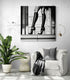 Intérieur contemporain avec un fauteuil blanc, un plaid foncé et un tableau en noir et blanc représentant des jambes féminines en talons aiguilles et chaussettes montantes. L’image joue sur l’élégance urbaine et le contraste graphique, créant une ambiance chic et audacieuse