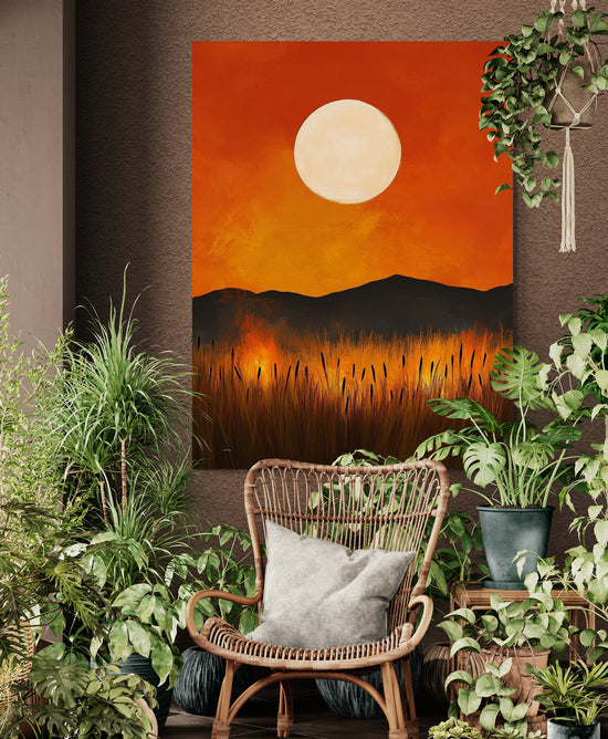 ableau de paysage en coucher de soleil accroché dans un espace de style bohème avec un fauteuil en rotin et une abondance de plantes d'intérieur, offrant une ambiance naturelle et chaleureuse.