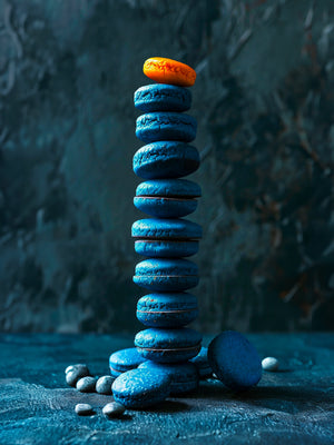 Pile de macarons bleus et orange sur fond abstrait bleu-gris.