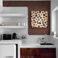 Tableau de grains de café sur fond crème, accroché sur un mur marron dans une cuisine moderne blanche avec des étagères flottantes.