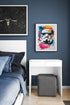 Une chambre avec un mur bleu foncé, un lit avec des draps bleus, et un petit bureau blanc. Deux tableaux sont accrochés : un casque de Stormtrooper coloré et un chasseur Y-wing sur un fond étoilé.