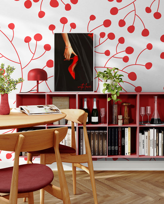 Un coin lecture avec des étagères rouges remplies de livres et de bouteilles. Un tableau représentant une main tenant un escarpin rouge est accroché sur un mur décoré de motifs rouges en forme de cerises.