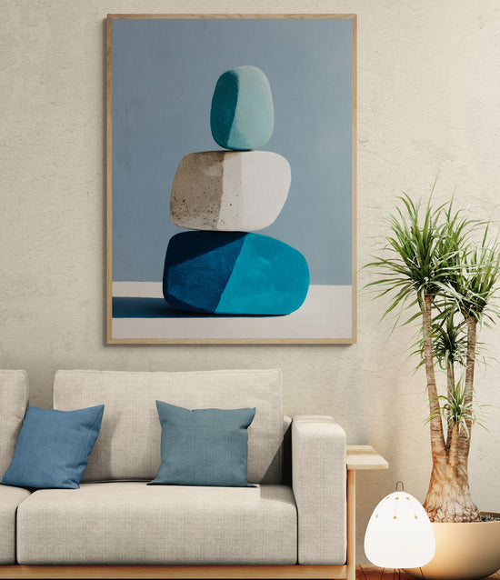 Grand tableau moderne représentant trois galets bleus et blancs empilés, accroché au-dessus d’un canapé beige avec coussins bleus, lampe design et plante verte dans un salon contemporain.