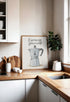 Tableau humoristique avec une cafetière italienne et la phrase « Espresso Yourself », posé sur un plan de travail en bois dans une cuisine scandinave lumineuse, décorée avec des bols blancs et une plante verte.