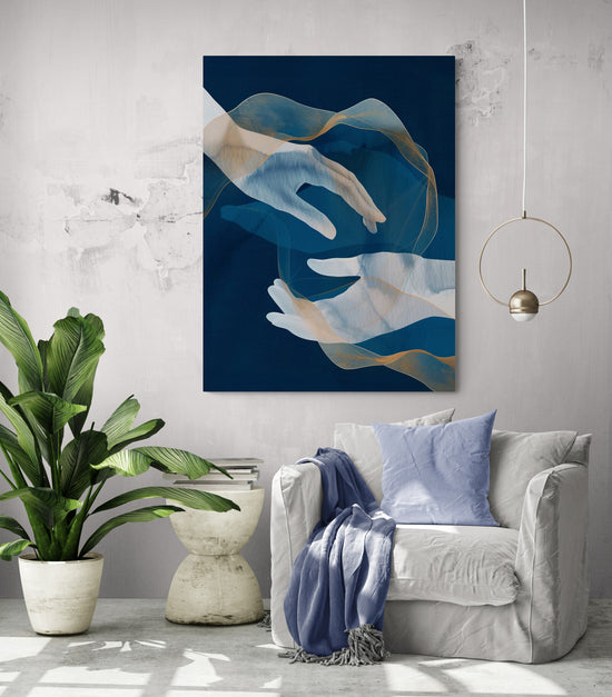 Un salon moderne avec un fauteuil blanc, une plante verte en pot à gauche et un tableau bleu représentant des mains et des voiles dorés sur le mur derrière.