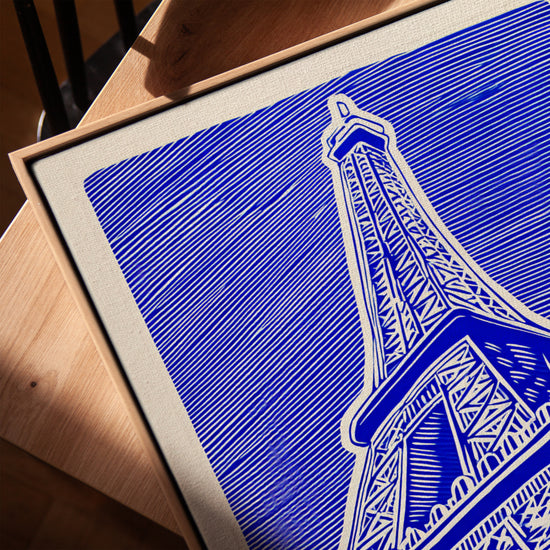 Tableau tour Eiffel bleu graphique moderne sur toile avec cadre chêne doré posé sur table salon