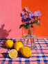 Tableau aux fleurs violettes et citrons jaunes sur fond rose et orange, style nature morte lumineuse