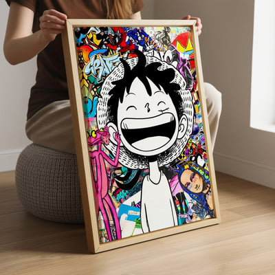 Une personne assise tient un tableau encadré représentant un personnage manga souriant sur un fond graffiti très coloré. Le cadre en bois repose sur ses genoux dans une pièce lumineuse.