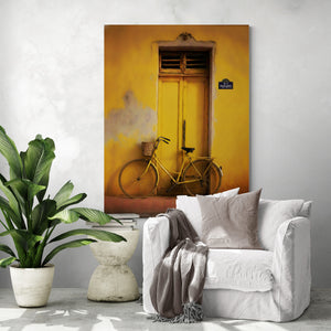 Tableau vélo vintage jaune sur mur jaune, au-dessus d’un fauteuil blanc dans un salon moderne.