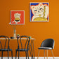 Dans une salle à manger les murs sont orange au centre une table et des chaises au style industriel. Accrochés au mur deux tableaux décorations murales de chat Maneki-neko sont accrochés au mur