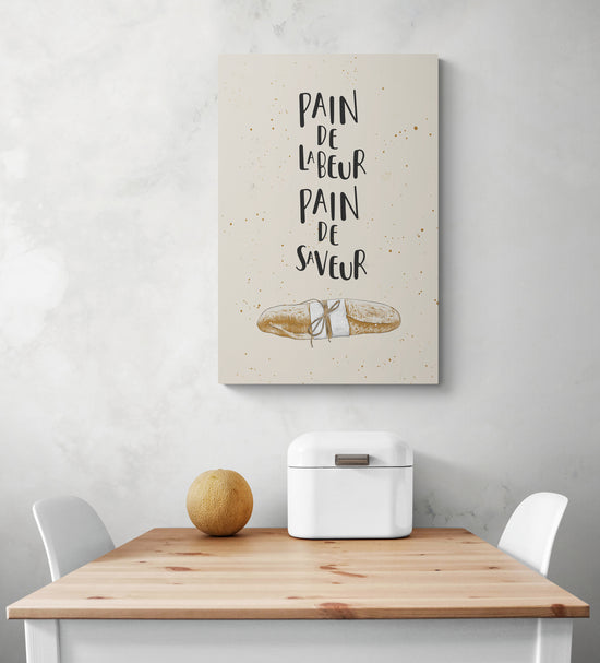 Tableau citation cuisine est suspendu au milieu d'une pièce blanche. Sur la photo sous le tableau se trouvent une table et deux chaises blanches.