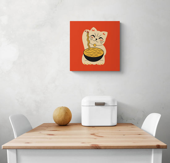 Un petit tableau cuisine avec un chat maneki-neko accroché sur un mur blanc. Dessous une table de repas et deux chaises blanches. Un melon et une boîte à pain sont sur la table.