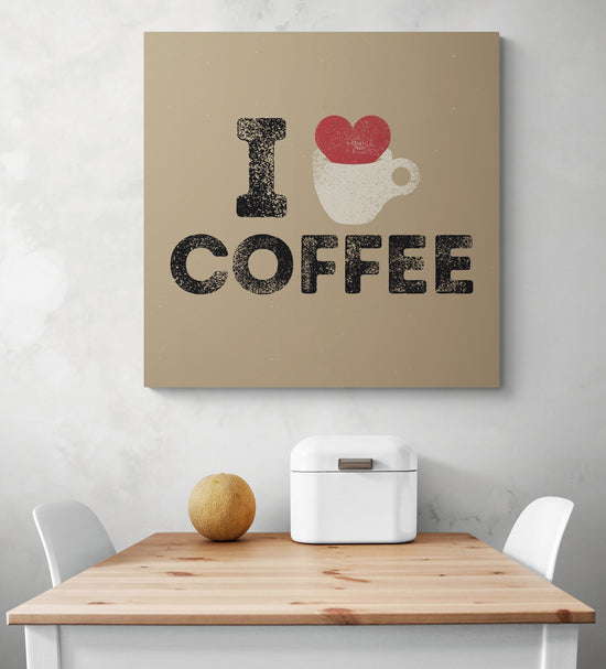 Tableau cuisine deco beige avec une illustration d'un cœur rouge qui déborde d'une tasse de café et une inscription en noir i love café, accroché sur un mur blanc