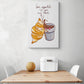  Un tableau décoration cuisine avec une l'illustration d'un croissant et chocolat chaud est accroché sur le mur blanc. Cette toile est placée au-dessus d'une table en bois et deux chaises sont de chaque côté. Une boîte à pain en métal blanc et un melon sont sur la table