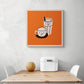 Un tableau deco pour cuisine orange est accroché sur le mur blanc. Ce tableau cuisine est placé au-dessus d'une table en bois et deux chaises sont de chaque côté. Une boîte à pain en métal blanc et un melon sont sur la table