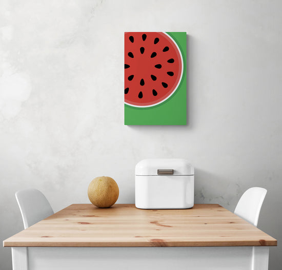 Un petit tableau deco pour cuisine est accroché sur le mur blanc, avec des couleurs vives, du rouge et du vert. En dessous du tableau de fruits se trouve une table et deux chaises blanches, qui semblent être en contraste avec les couleurs vibrantes du tableau. Sur la table se trouve une corbeille à pain en métal blanc et un petit melon. Tous ces éléments créent un look frais et coloré dans la pièce.